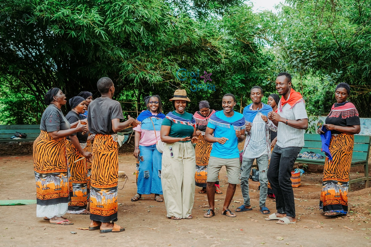 Group of people in traditional and casual clothing dancing outdoors with greenery in the background
