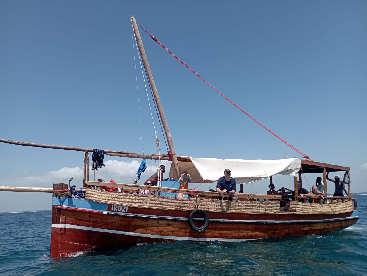 Traditional wooden boat on water with people on board under a clear blue sky.