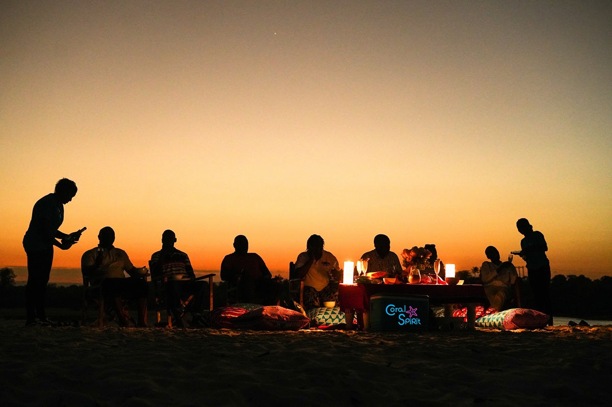 Silhouettes of people sitting around a campfire at sunset on Kongo river beach.
