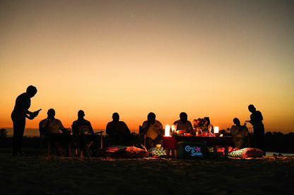 Silhouettes of people sitting around a campfire at sunset on Kongo river beach.