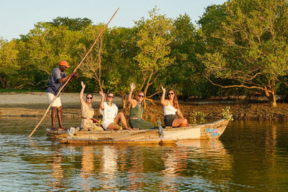 Group of people on a dug-out canoe in a natural setting with mangrove trees along a river.