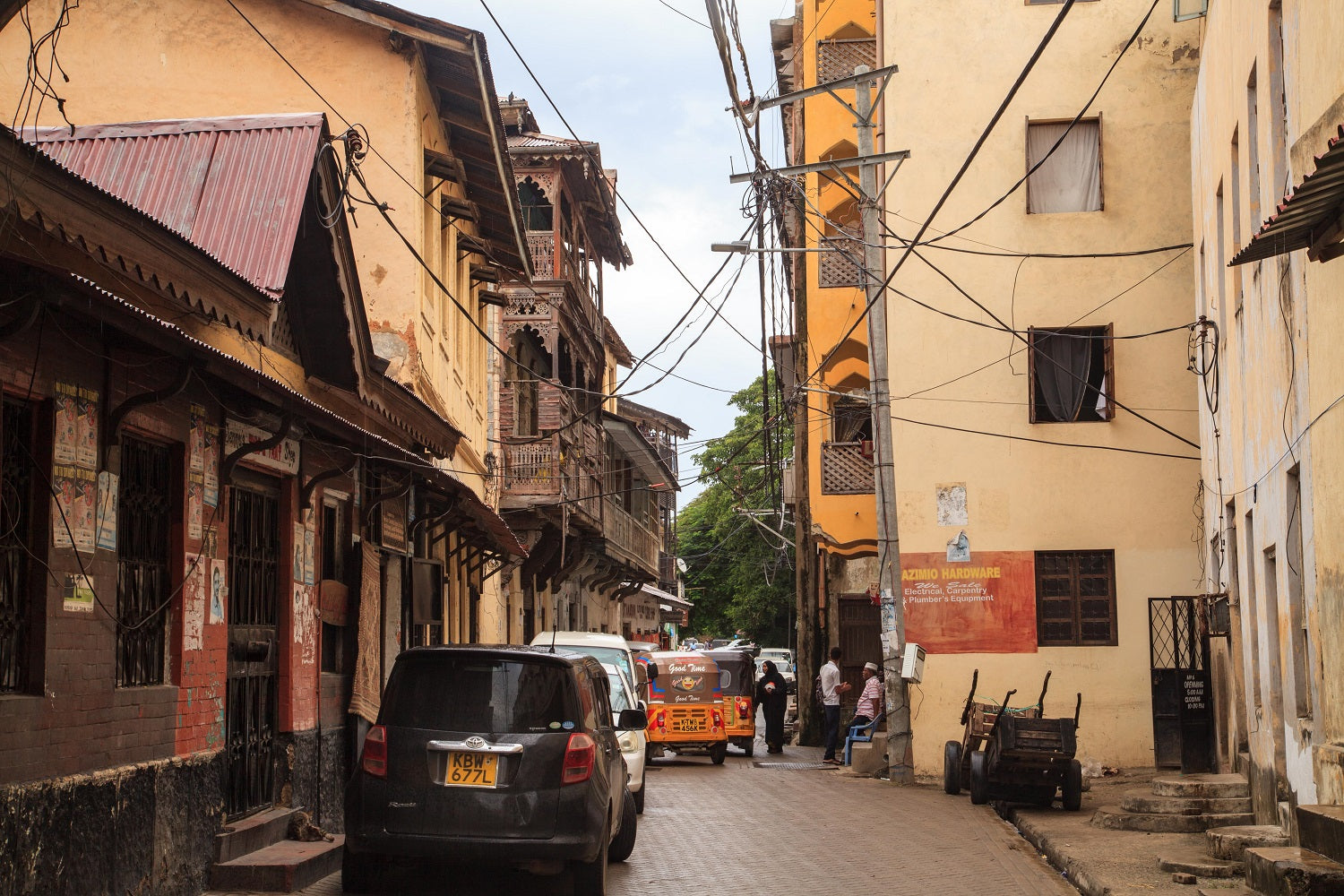 Old buildings crisscrossed with wires with a line of cars on a paved road