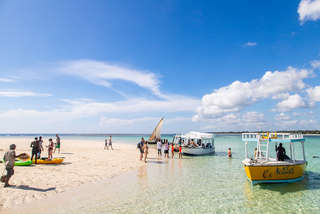 Beach scene with people, boats, and clear blue sky in Diani, Kenya.