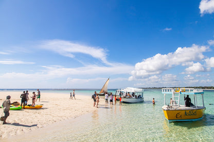 Beach scene with people, boats, and clear blue sky in Diani, Kenya.
